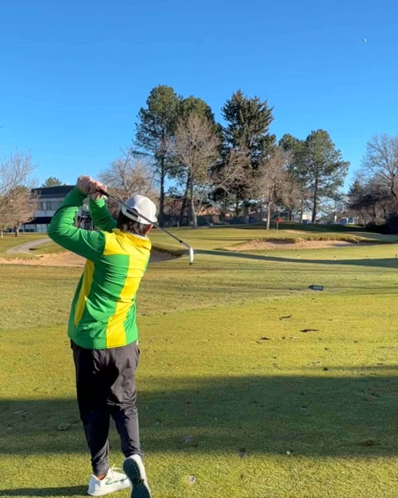 A golfer holds the finish after an iron shot on a sunny winter fairway